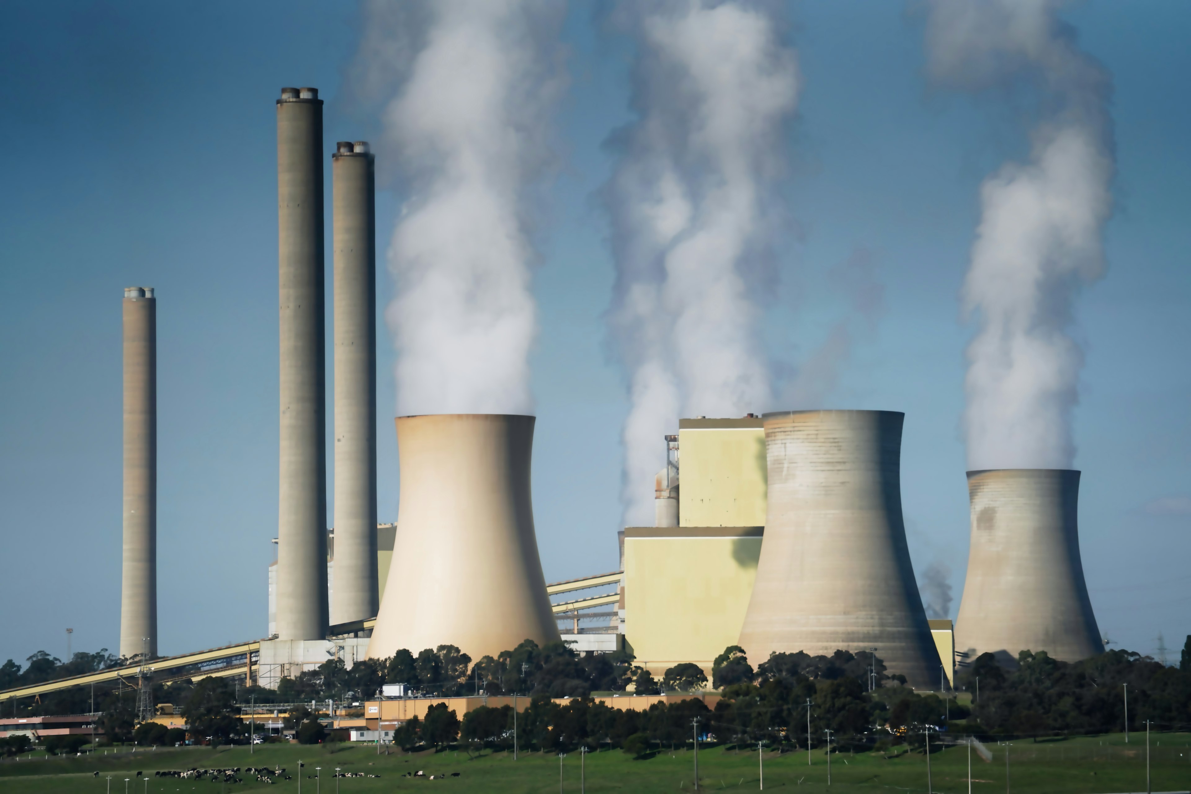 Coal-fired power plant with smokestacks and cooling towers emitting plumes over a green field